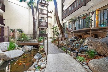 A small pond with rocks and a wooden bridge in the middle of a courtyard.